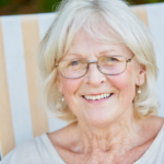 A cheerful elderly woman with white hair and glasses, smiling broadly, representing the satisfaction of customers who use the chimney cleaning services offered by ohmycleaners.com in Omaha